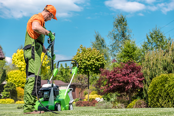 Caucasian Professional Gardener Taking Care of His Working Equipment. Pressure Washing Gasoline Grass Mower in Beautiful Garden.